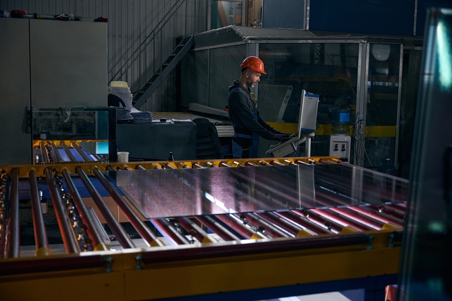Trabajador supervisando una línea de producción industrial durante una de las etapas clave de cómo se fabrica el vidrio en plantas automatizadas.