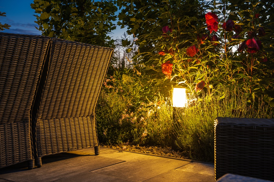 Baliza de luz cálida instalada junto a plantas en una terraza ajardinada, ejemplo de iluminación exterior para terrazas funcional y decorativa.
