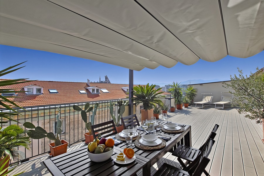 Terraza decorada con plantas en macetas y comedor exterior bajo un toldo retráctil. Imagen que muestra cómo poner un toldo en una terraza para generar un ambiente confortable y sombreado.