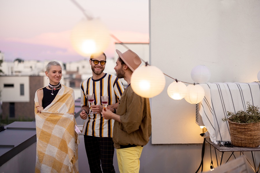 Decoración exterior terraza con guirnaldas de luz cálida, grupo de personas conversando al atardecer en una azotea urbana con ambiente acogedor