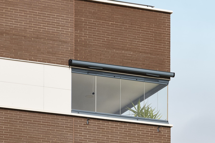 Balcón cerrado con vidrio transparente y marco superior abatible en edificio de ladrillo. Ejemplo funcional dentro de las mejores ideas para cerrar un balcón manteniendo luminosidad.