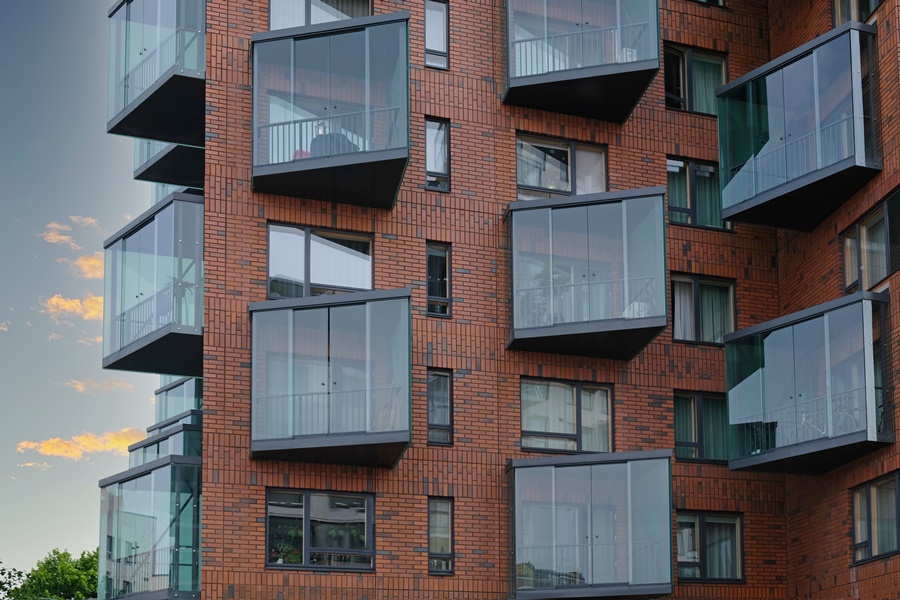 Fachada de edificio contemporáneo con balcones acristalados en esquina, todos cerrados con cristal sin perfilería visible. Solución arquitectónica ideal entre las ideas para cerrar un balcón sin perder claridad.